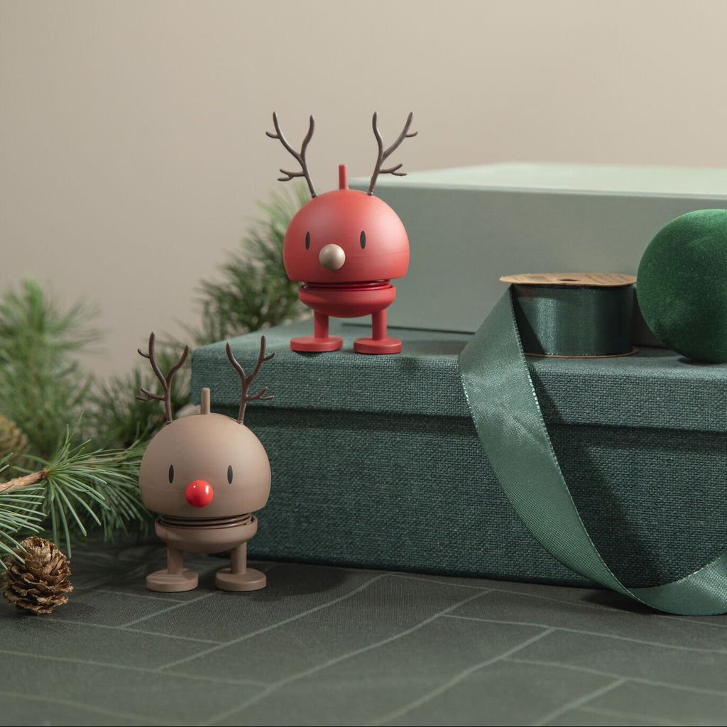 Two small figurines with antlers on a textured surface with greenery and ribbons.