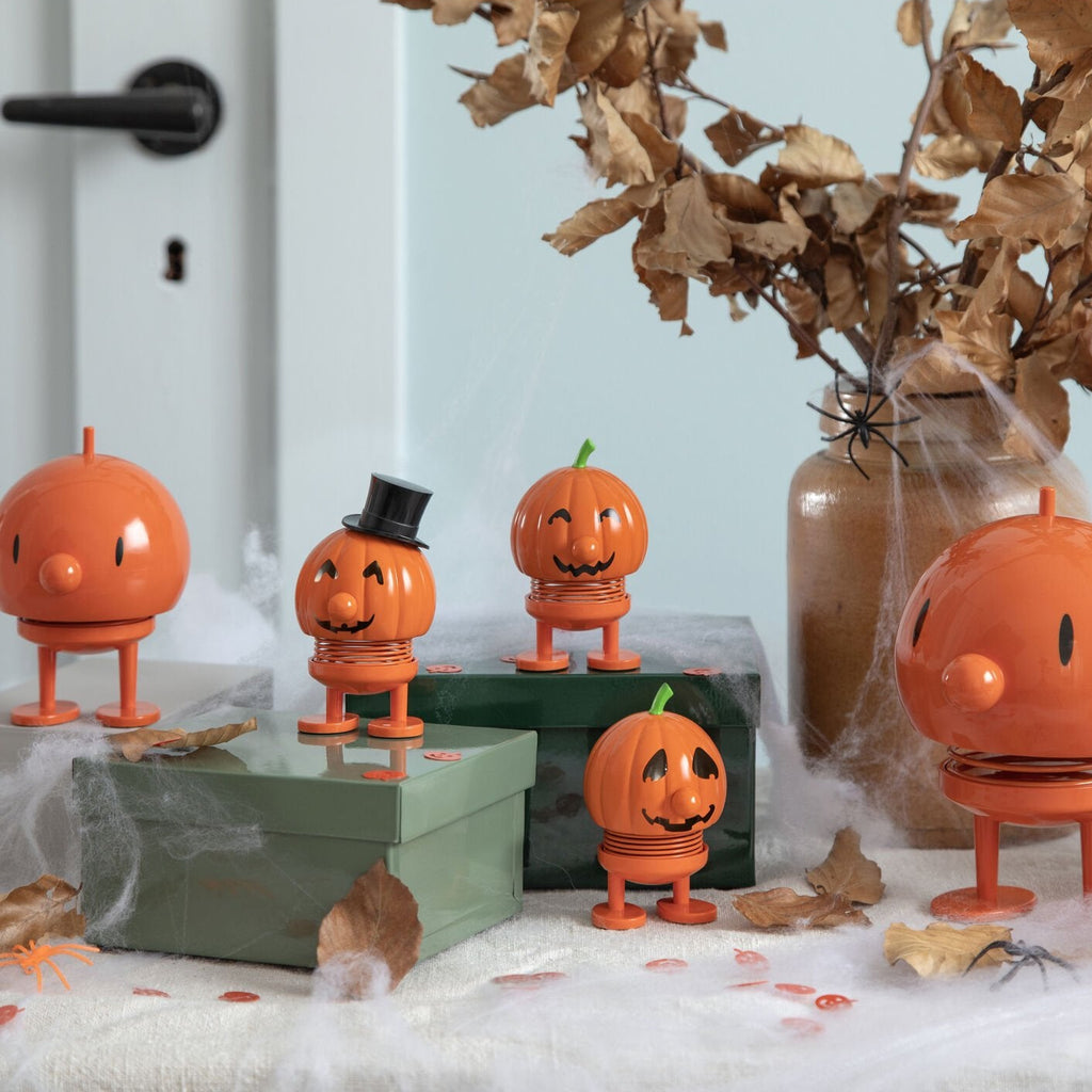 Set of orange jack-o'-lantern figurines on a decorative surface with spider webs and leaves.