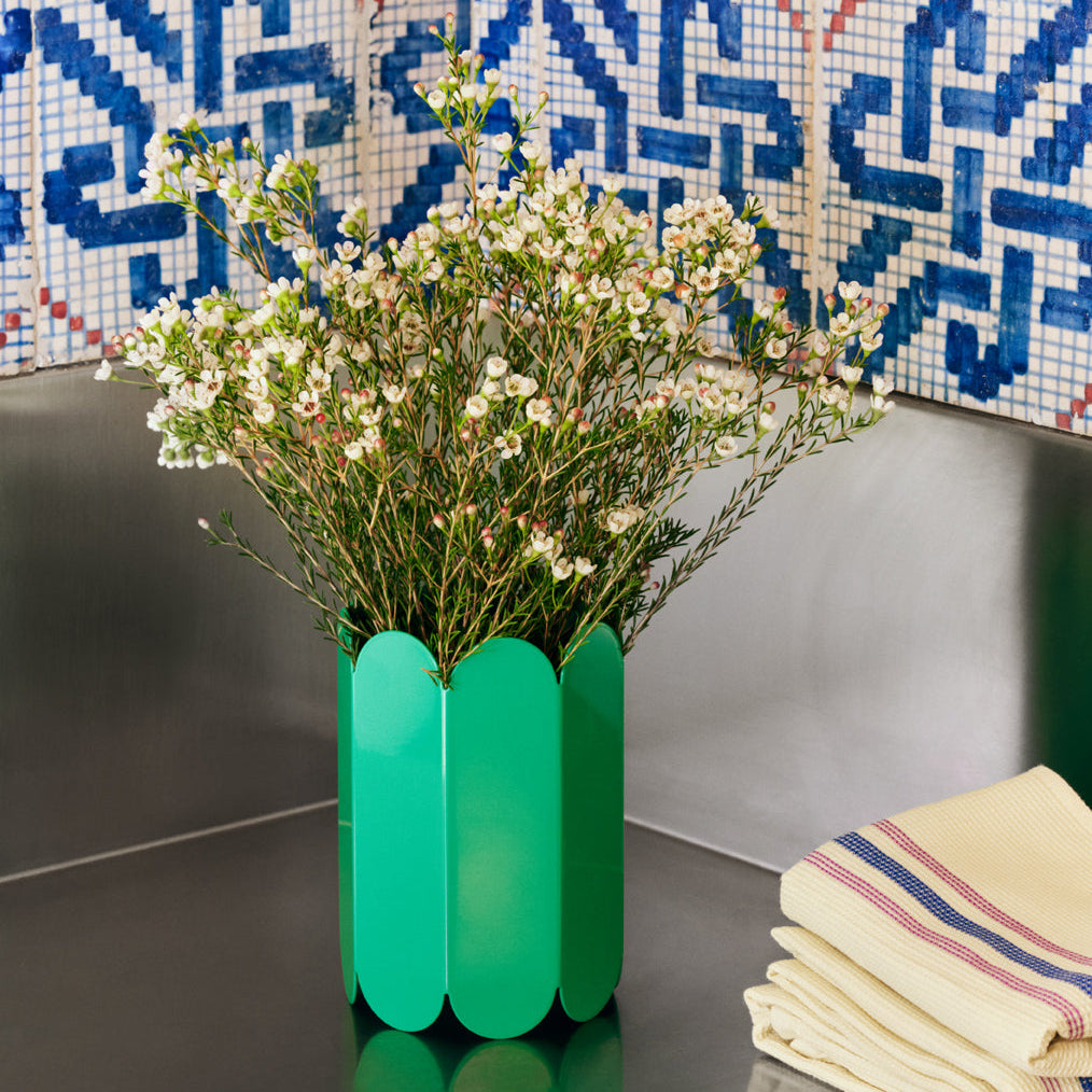 Green vase with flowers on a table against a mosaic wall