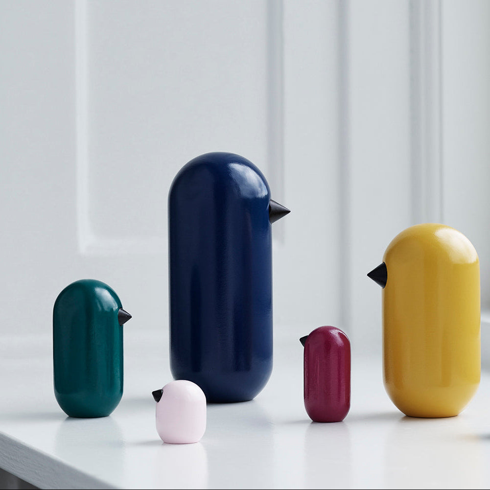 Colourful bird-shaped objects on a white surface with a light gray wall in the background