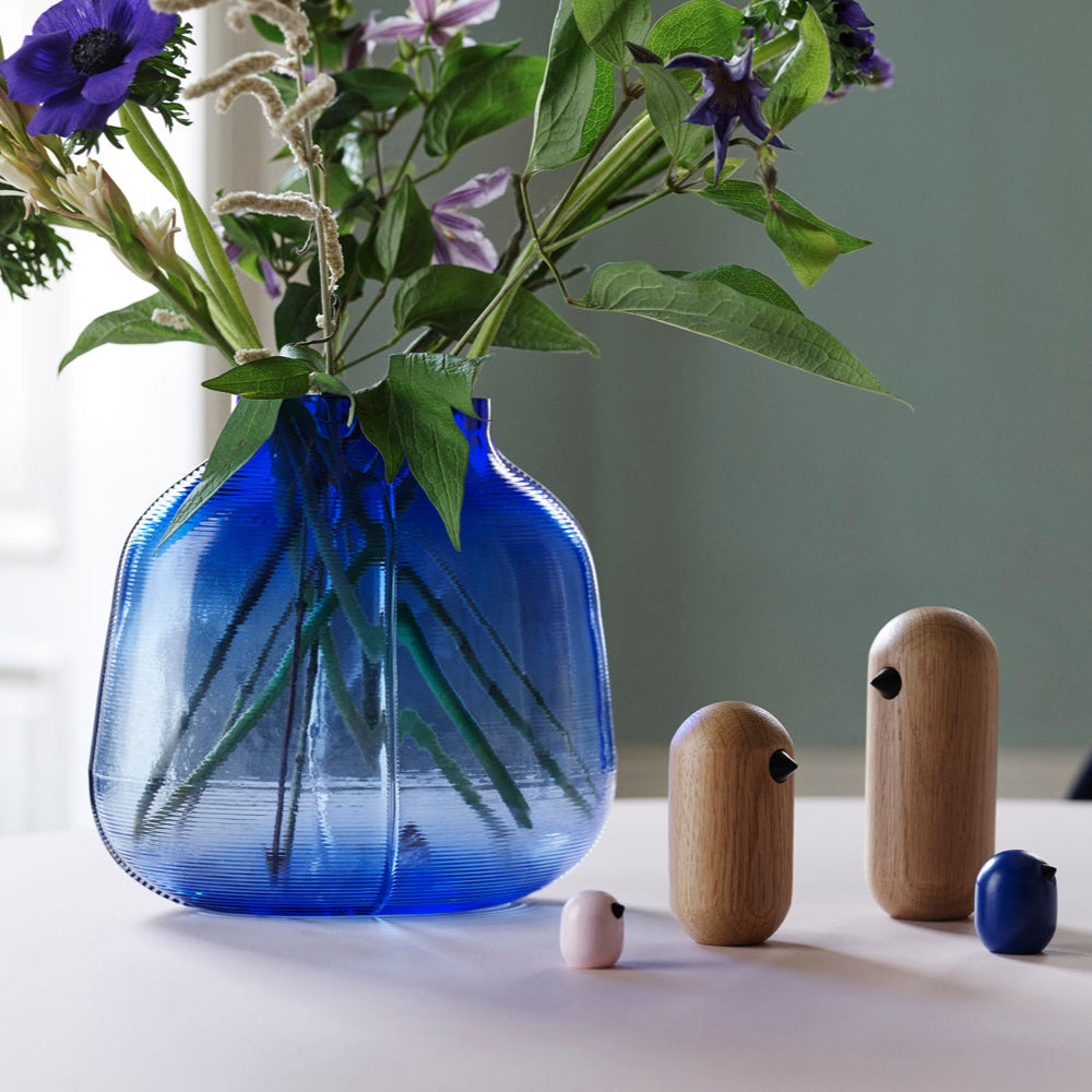 Blue vase with flowers on a table with wooden sculptures and a small blue object.