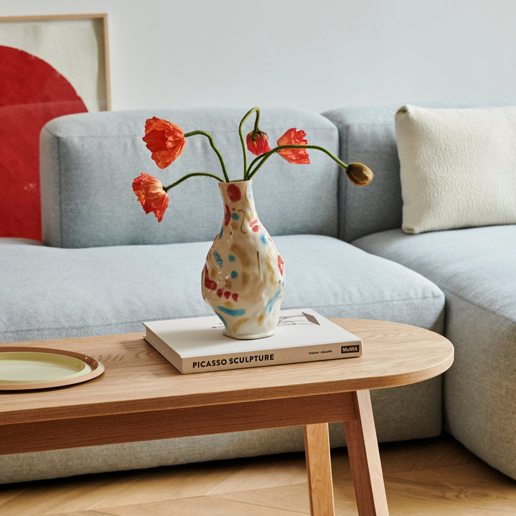 Vase with red flowers on a wooden coffee table in a living room setting.