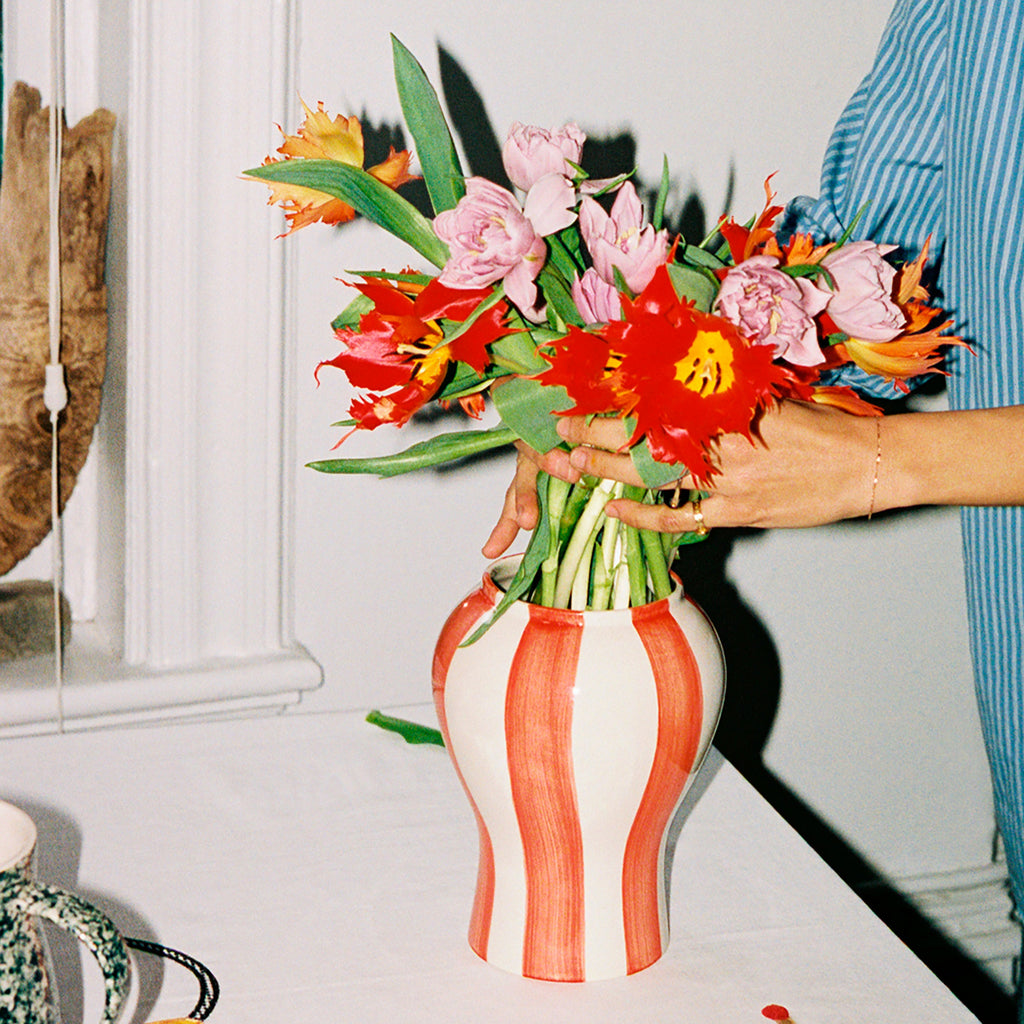 Person holding a bouquet of flowers next to a striped vase on a table.