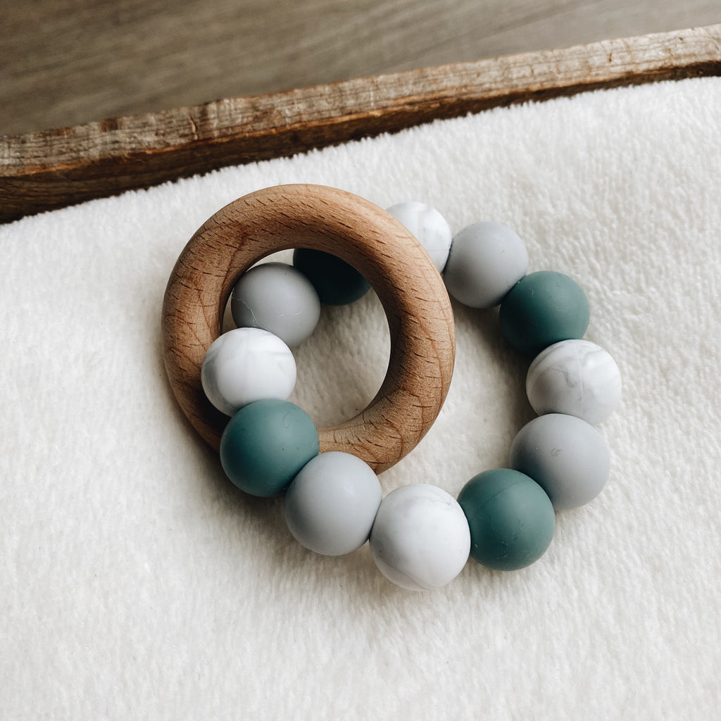 Baby teether in grey blue, white and grey with a wooden ring.