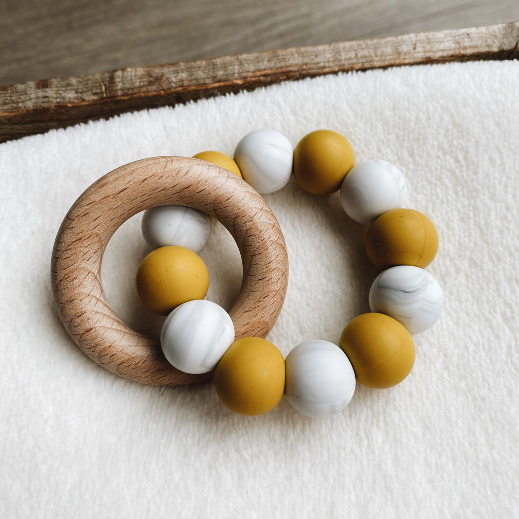 Baby teether in yellow ochre, white and grey with a wooden ring.